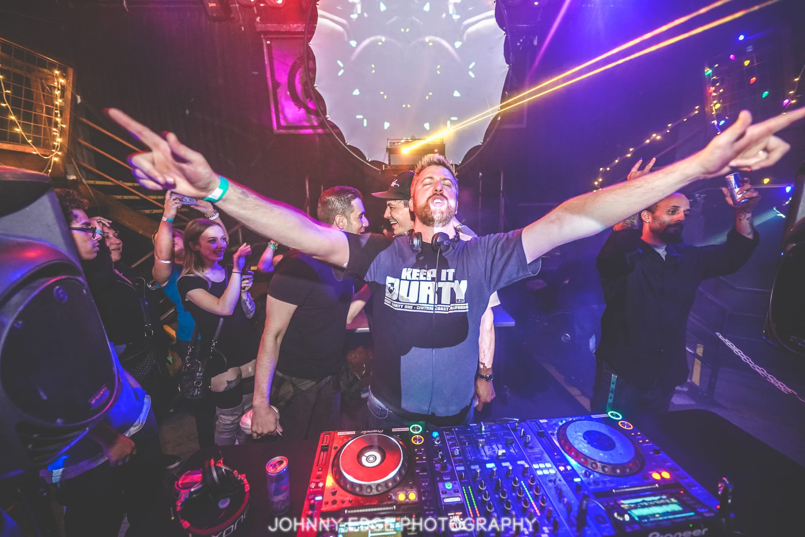 Durty behind the decks with both arms raised, lasers overhead and the crowd pressed in on all sides